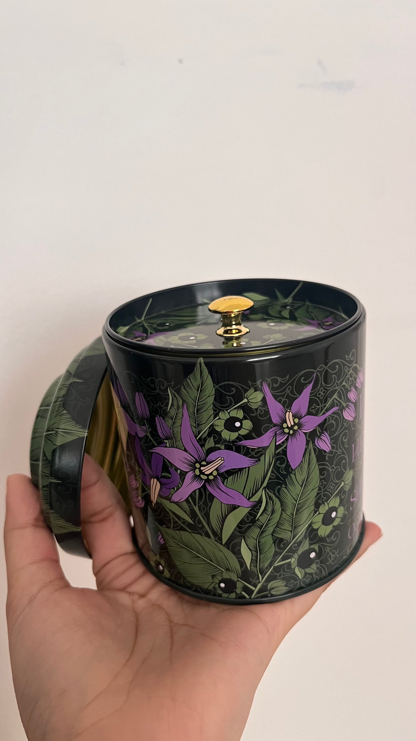 Hand holding a black candle jar with floral design against a white background