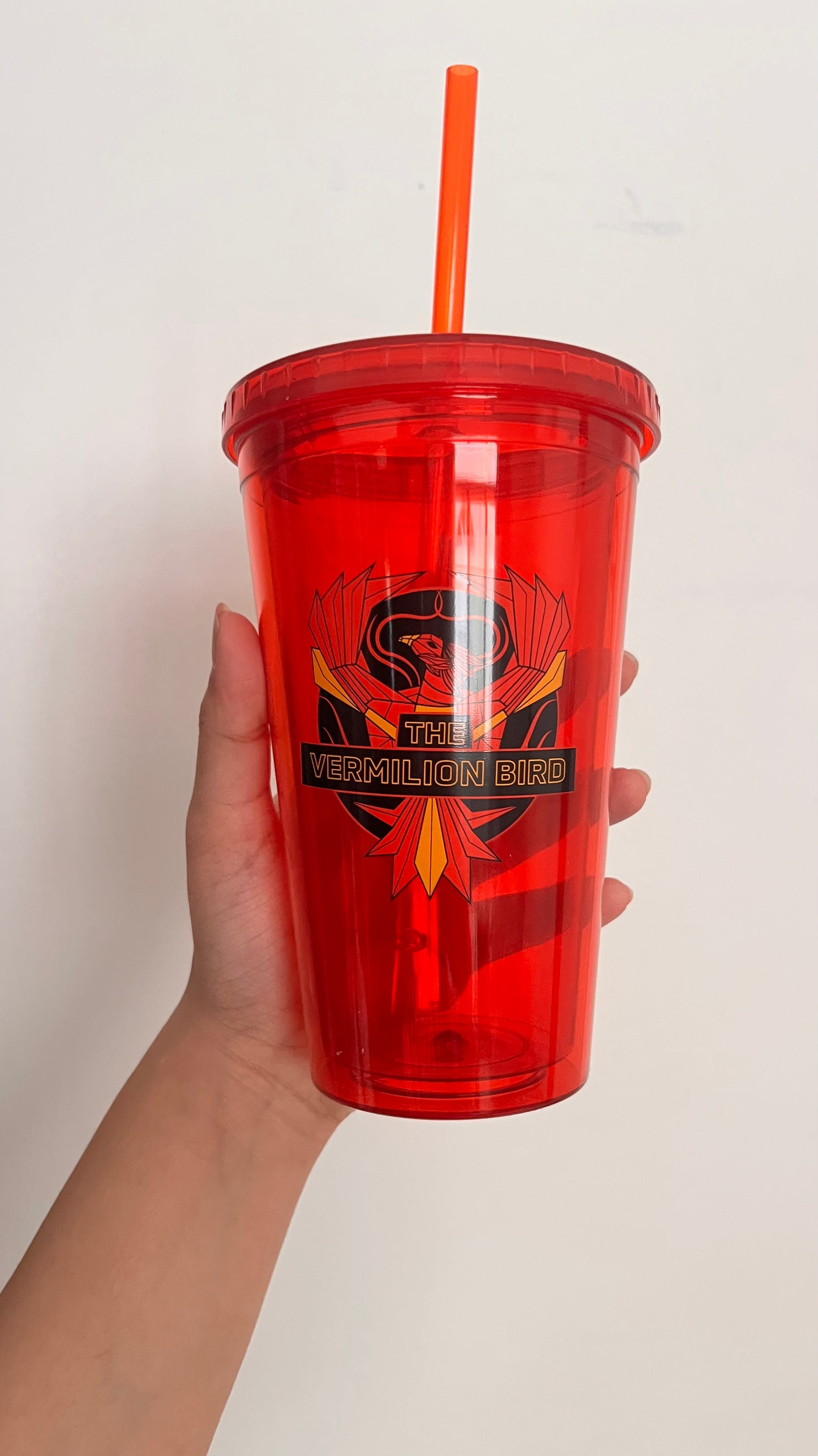 Red tumbler with a logo and straw held by a hand against a plain background