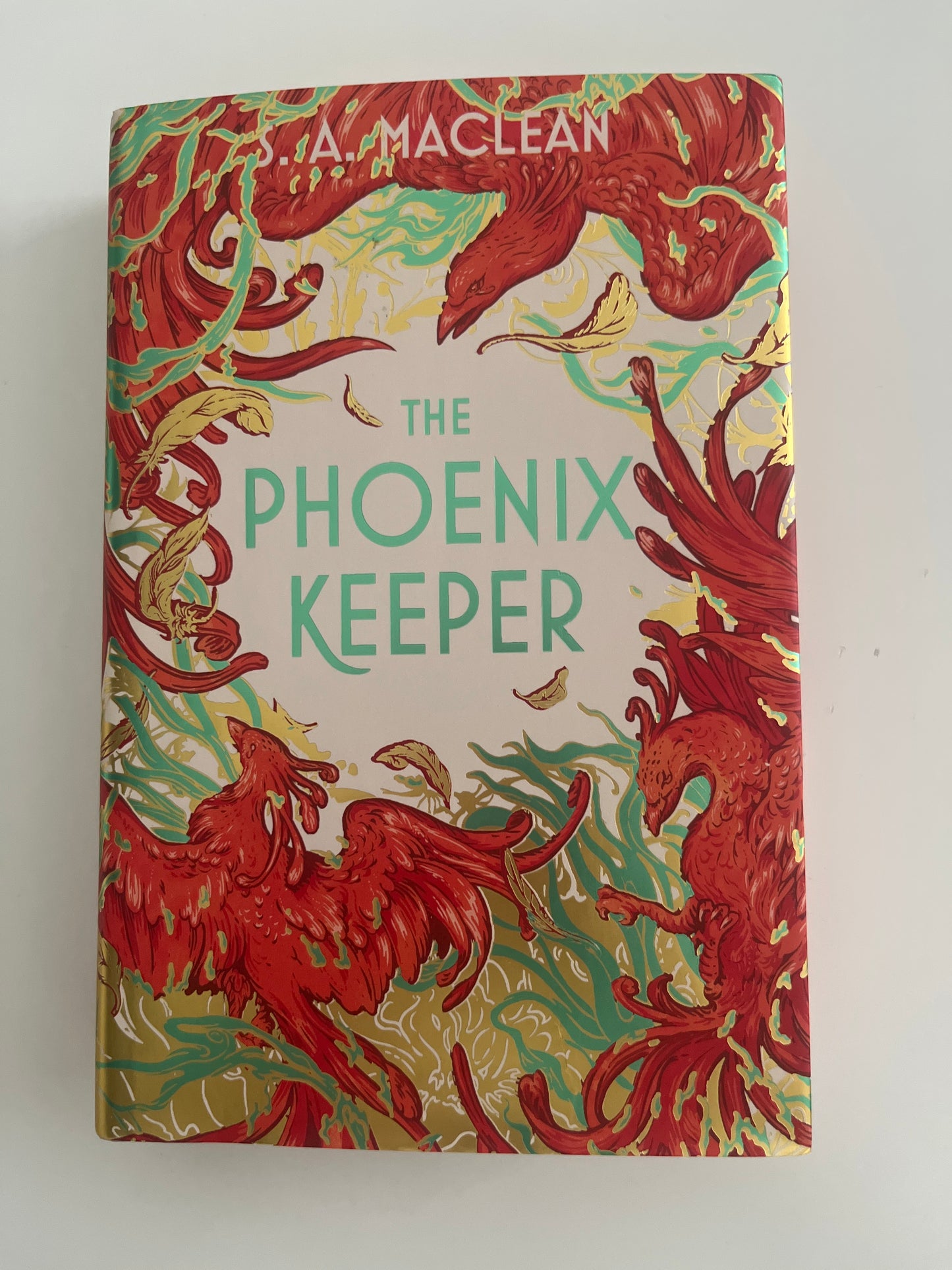 Book cover of 'The Phoenix Keeper' with red phoenix illustrations on a beige background