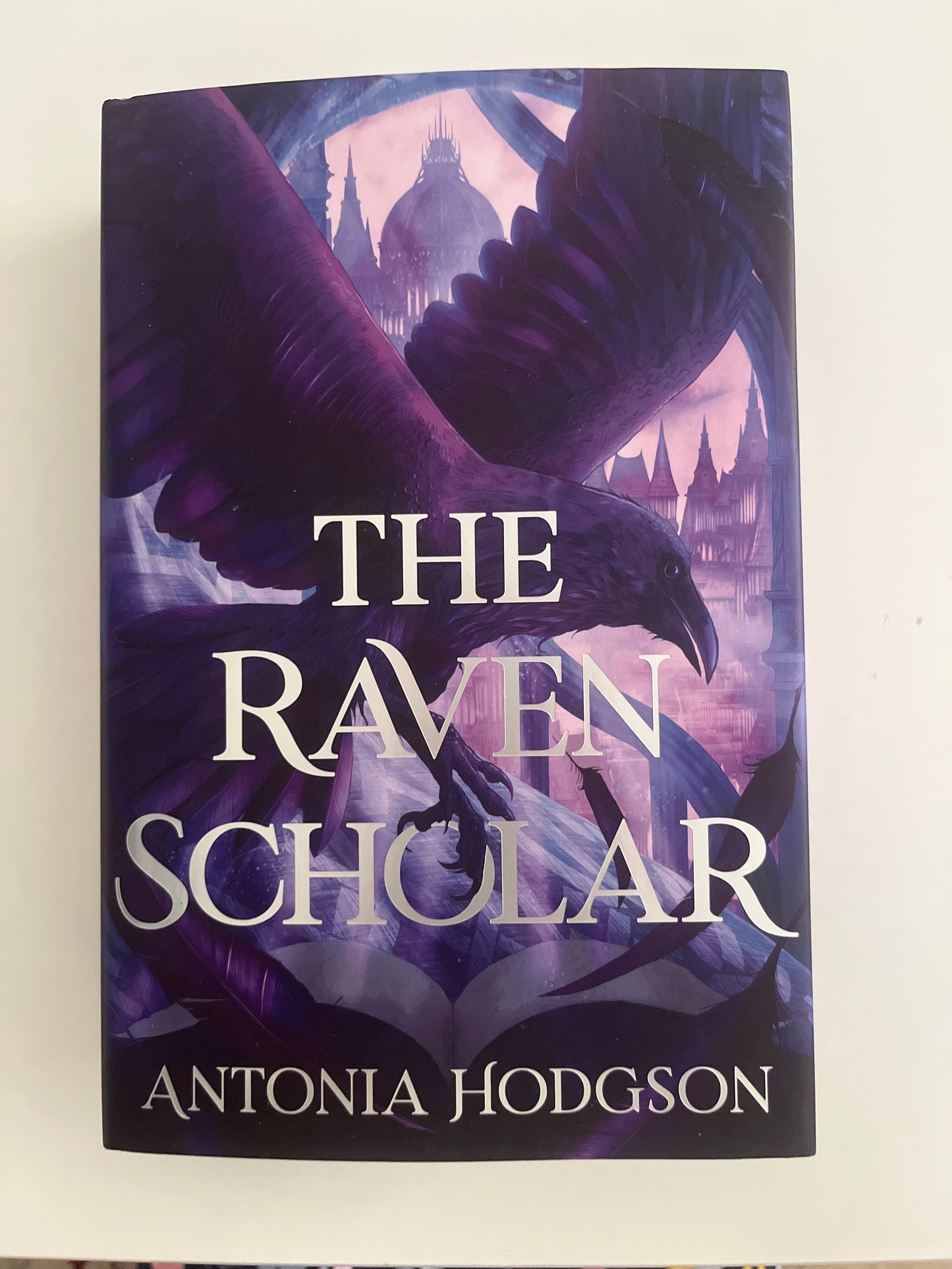 Book cover of 'The Raven Scholar' by Antonia Hodgson with a purple and black design.