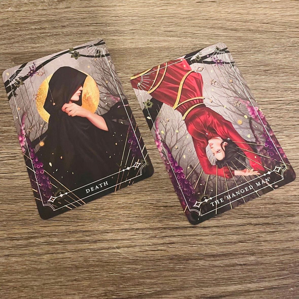 Two tarot cards, 'Death' and 'The Hanged Man', on a wooden surface.