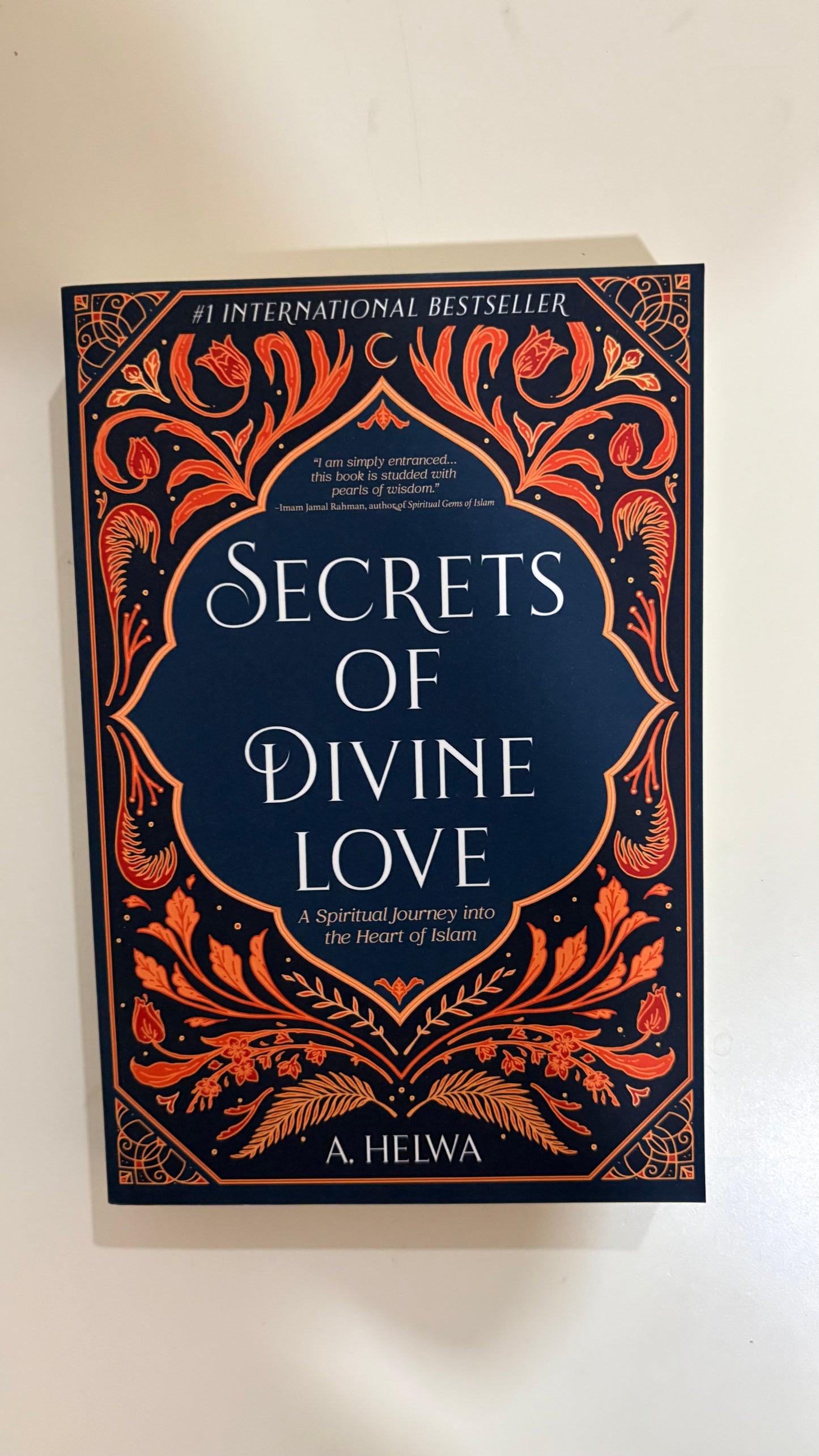 The book cover of 'Secrets of Divine Love' by A. Helwa, featuring a dark navy blue background with intricate orange and gold ornate border designs and white text.
