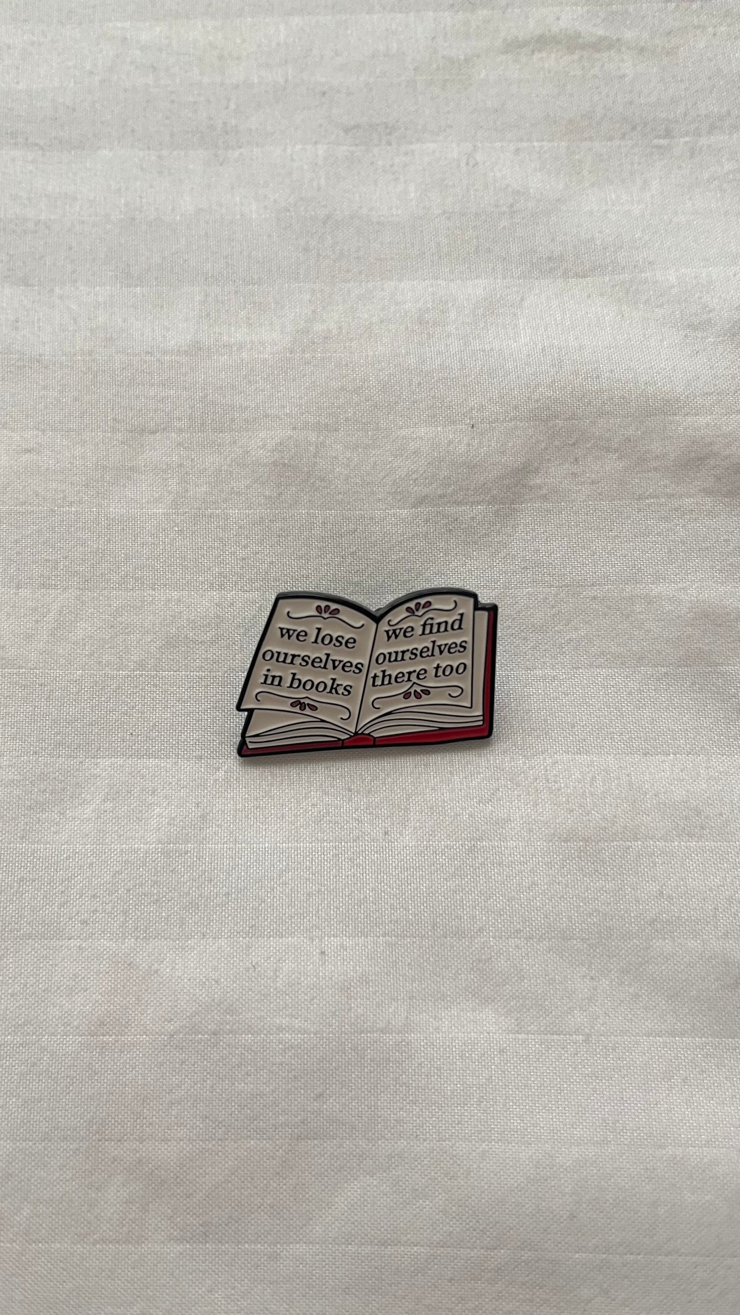 Enamel pin with quote: "We lose ourselves in books, we find ourselves there too"
