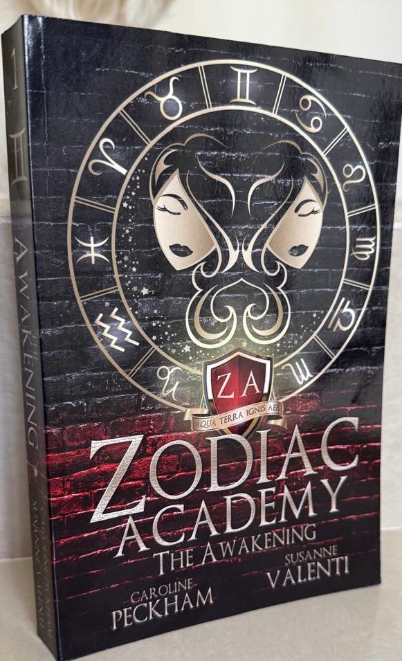 Book titled 'Zodiac Academy: The Awakening' with zodiac symbols on the cover.