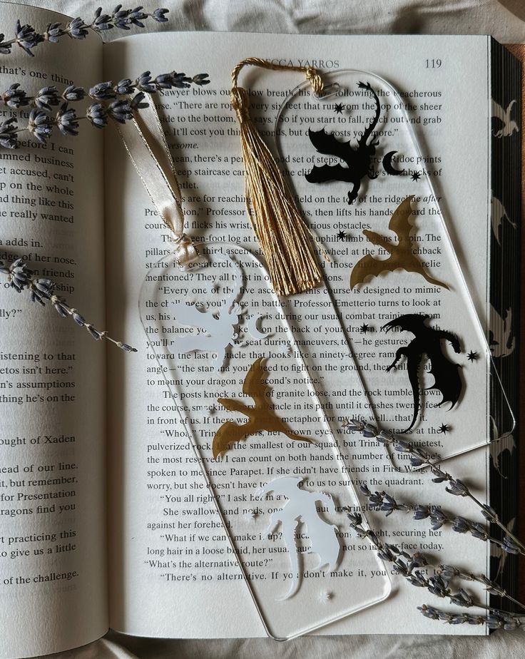 Acrylic bookmarks with floral and bookish designs laid out beside an open book foruth wing with dragons