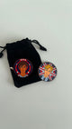 Two round pins with illustrated characters on a black drawstring bag against a white background
