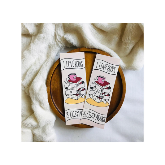 Two bookmarks with a cup of tea and book design on a wooden plate with a soft fabric background.