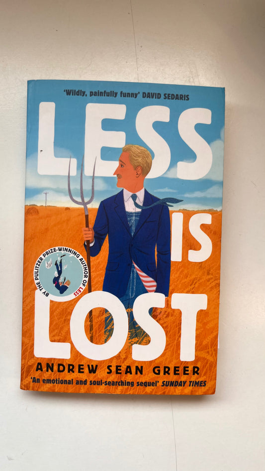 Book cover of 'Less is Lost' by Andrew Sean Greer on a white wall.
