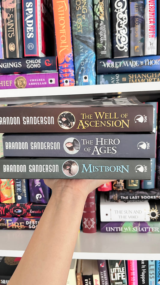 Stack of books by Brandon Sanderson on a bookshelf with other books.