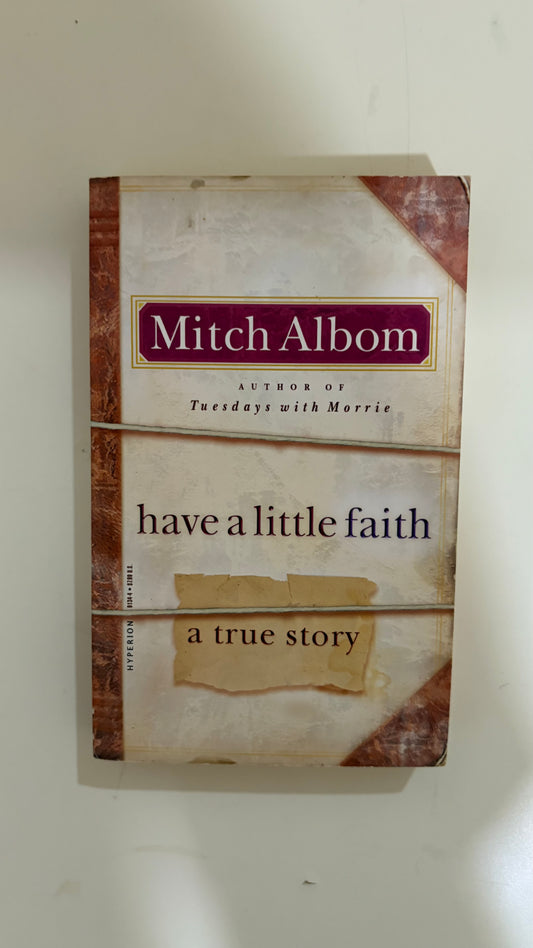 A paperback copy of Mitch Albom's book 'have a little faith: a true story' resting on a light-colored surface.