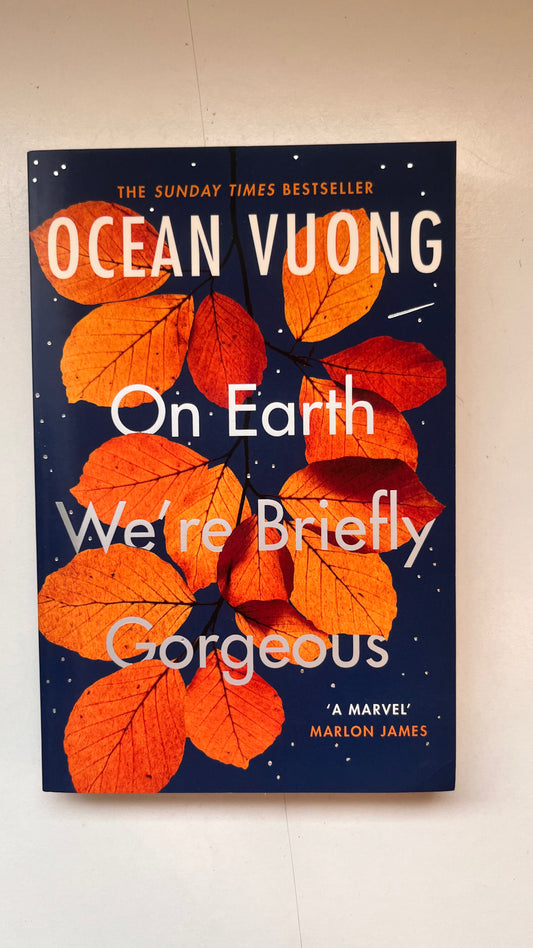 Book cover of 'On Earth We're Briefly Gorgeous' by Ocean Vuong with orange leaves on a dark blue background.