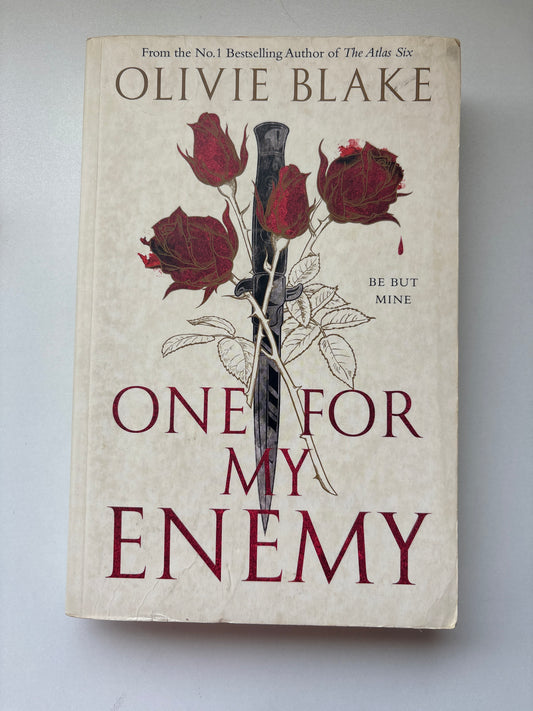 The front cover of the book 'One For My Enemy' by Olivie Blake, featuring a beige background with dark red roses, a black-and-white dagger, and dark red title text.
