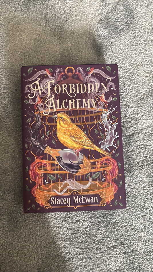 Book titled 'A Forbidden Alchemy' by Stacey McTwan on a textured surface