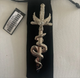 Decorative metal object with eagle and snake design on a black stand against a light background