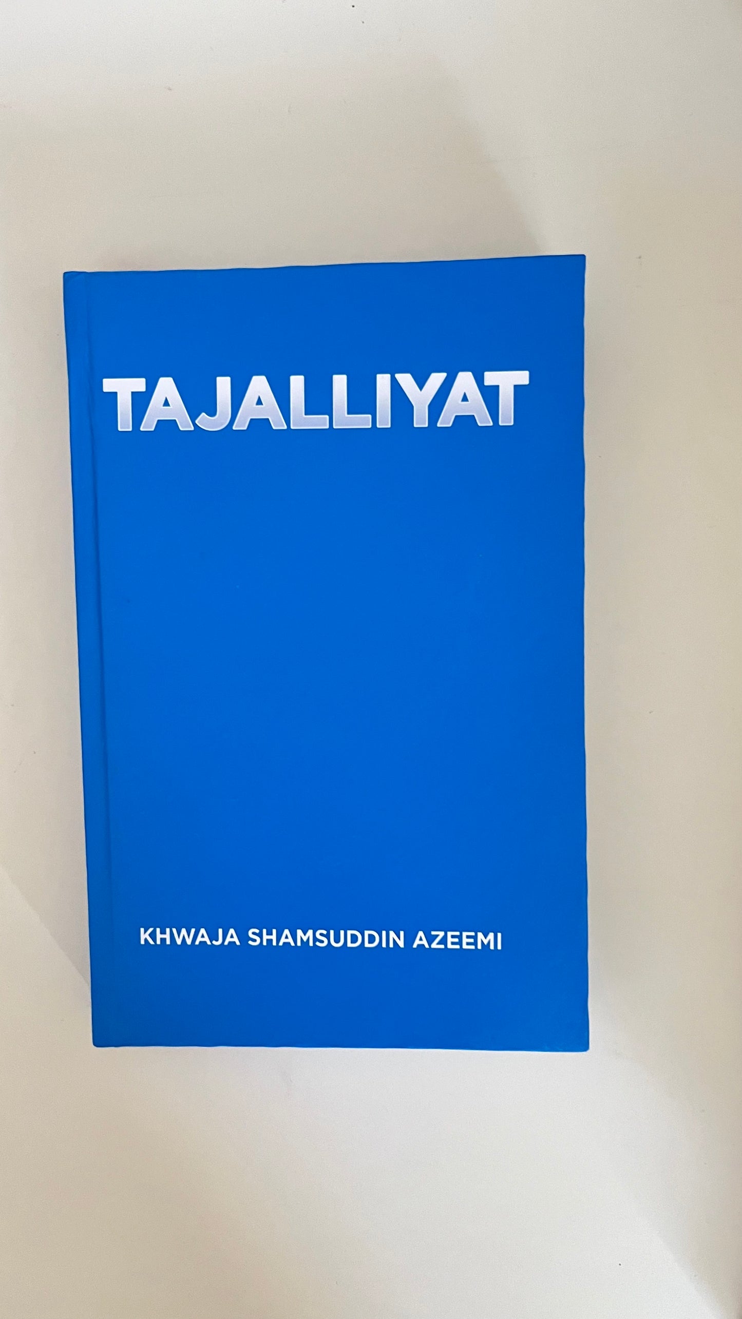 Paperback of Tajalliyat by Khawaja Shamsuddin Azeemi with luminous design elements symbolizing spiritual illumination.

