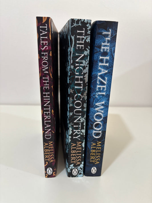 Three books stacked on a white surface with visible author and title text.