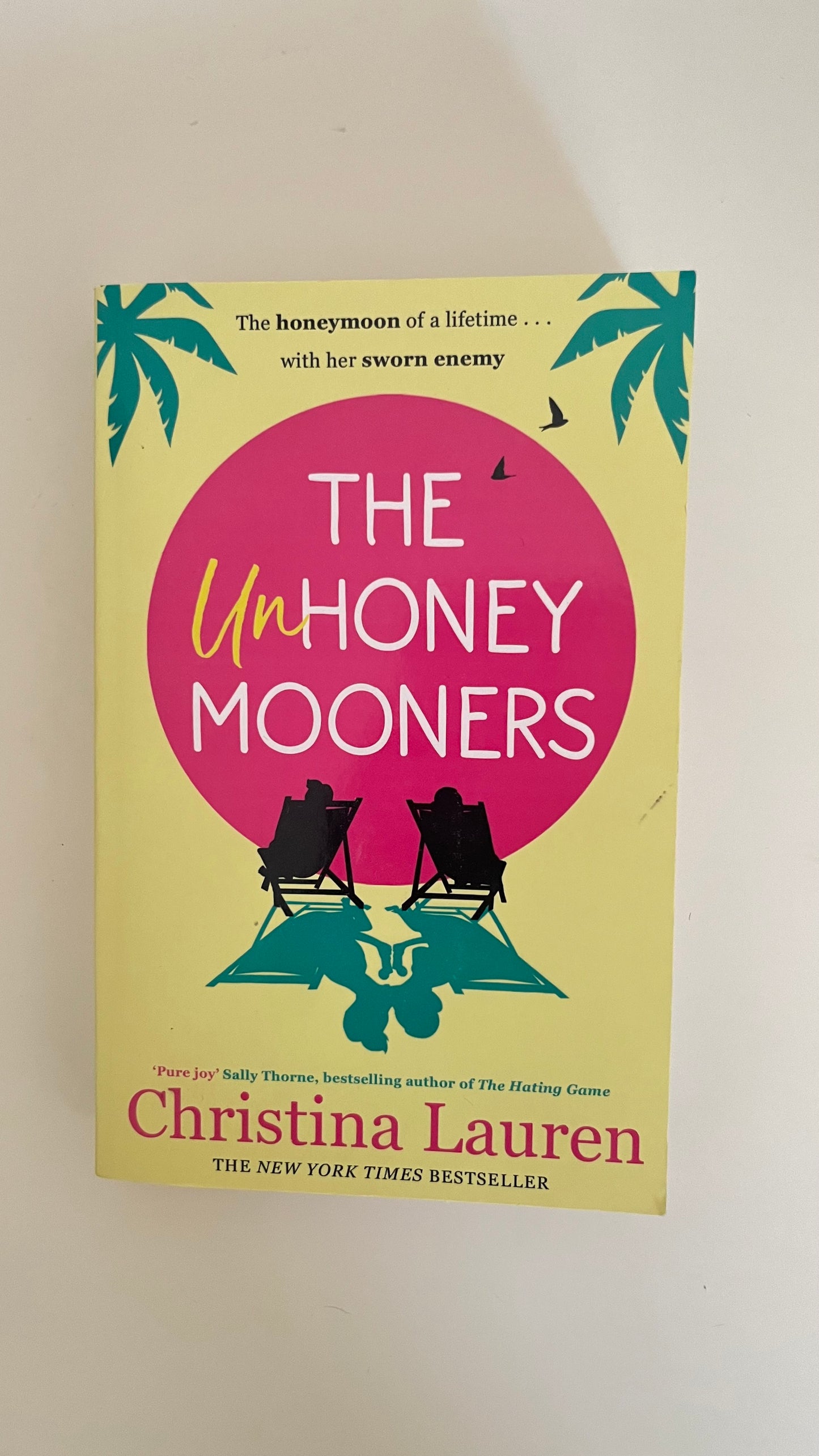 Paperback of The Unhoneymooners by Christina Lauren with playful and bright cover design.

