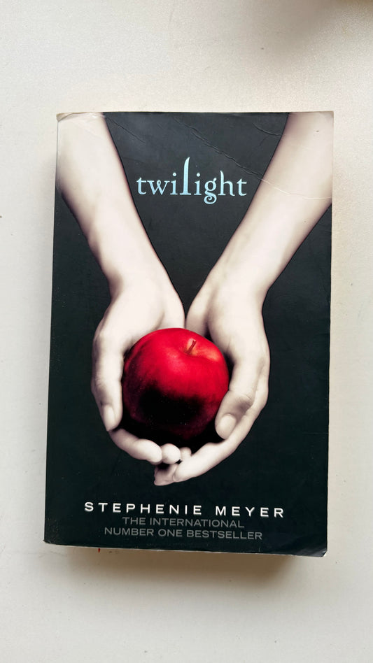 Book cover of 'Twilight' by Stephenie Meyer with hands holding a red apple on a white background