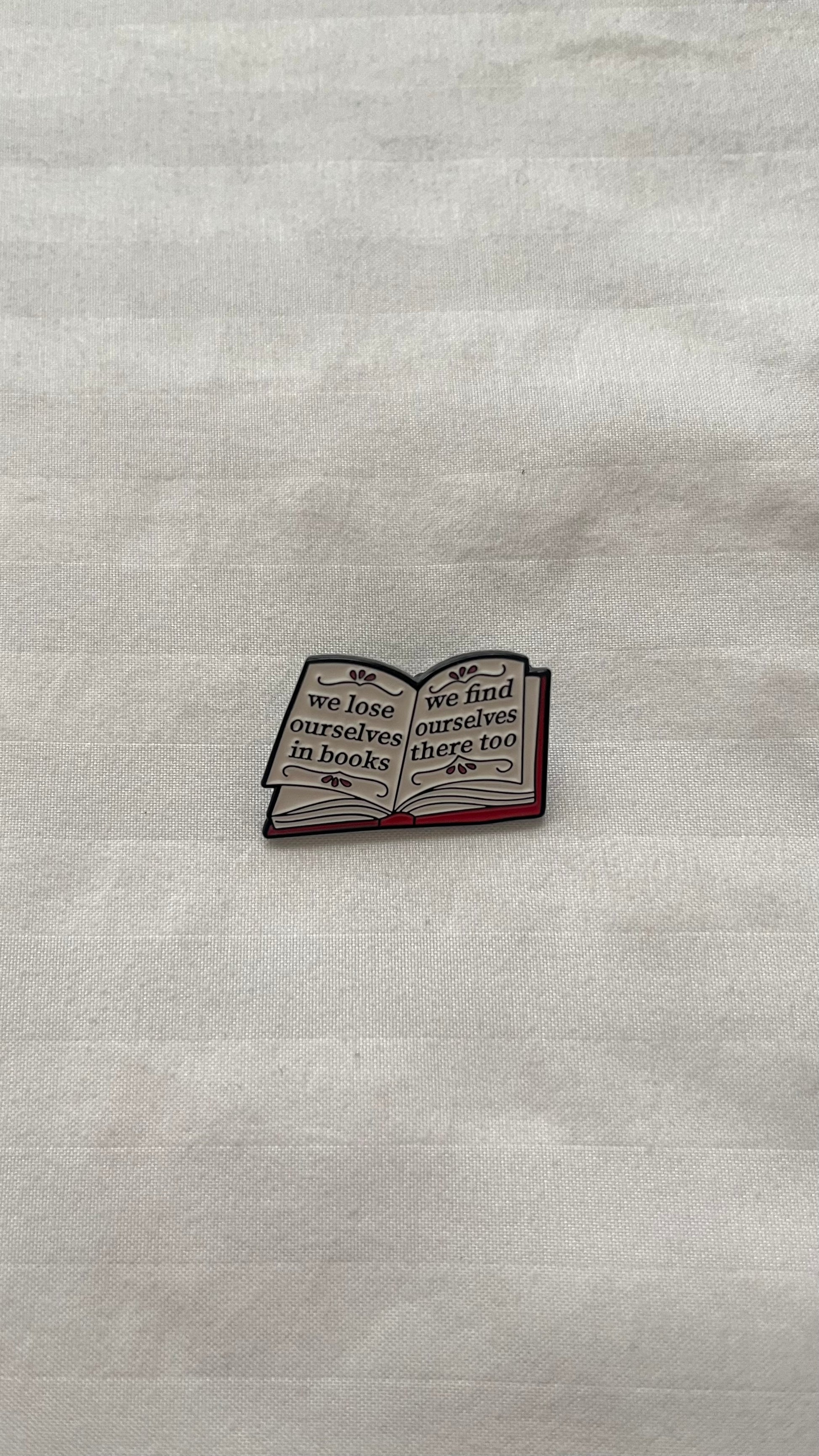 Enamel pin with quote: "We lose ourselves in books, we find ourselves there too"