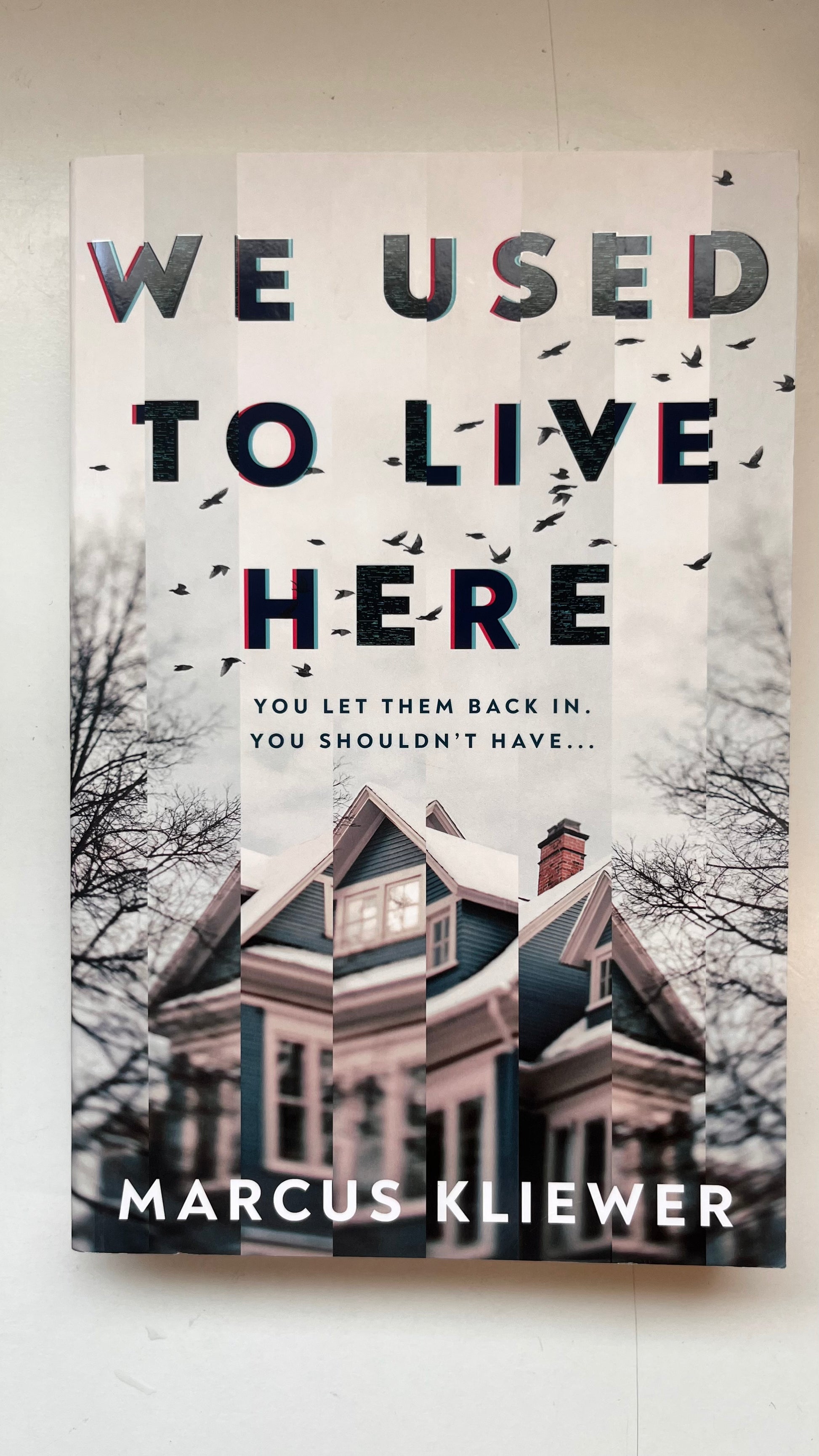 Book cover of 'We Used to Live Here' by Marcus Kliewer with a house and trees in the background.