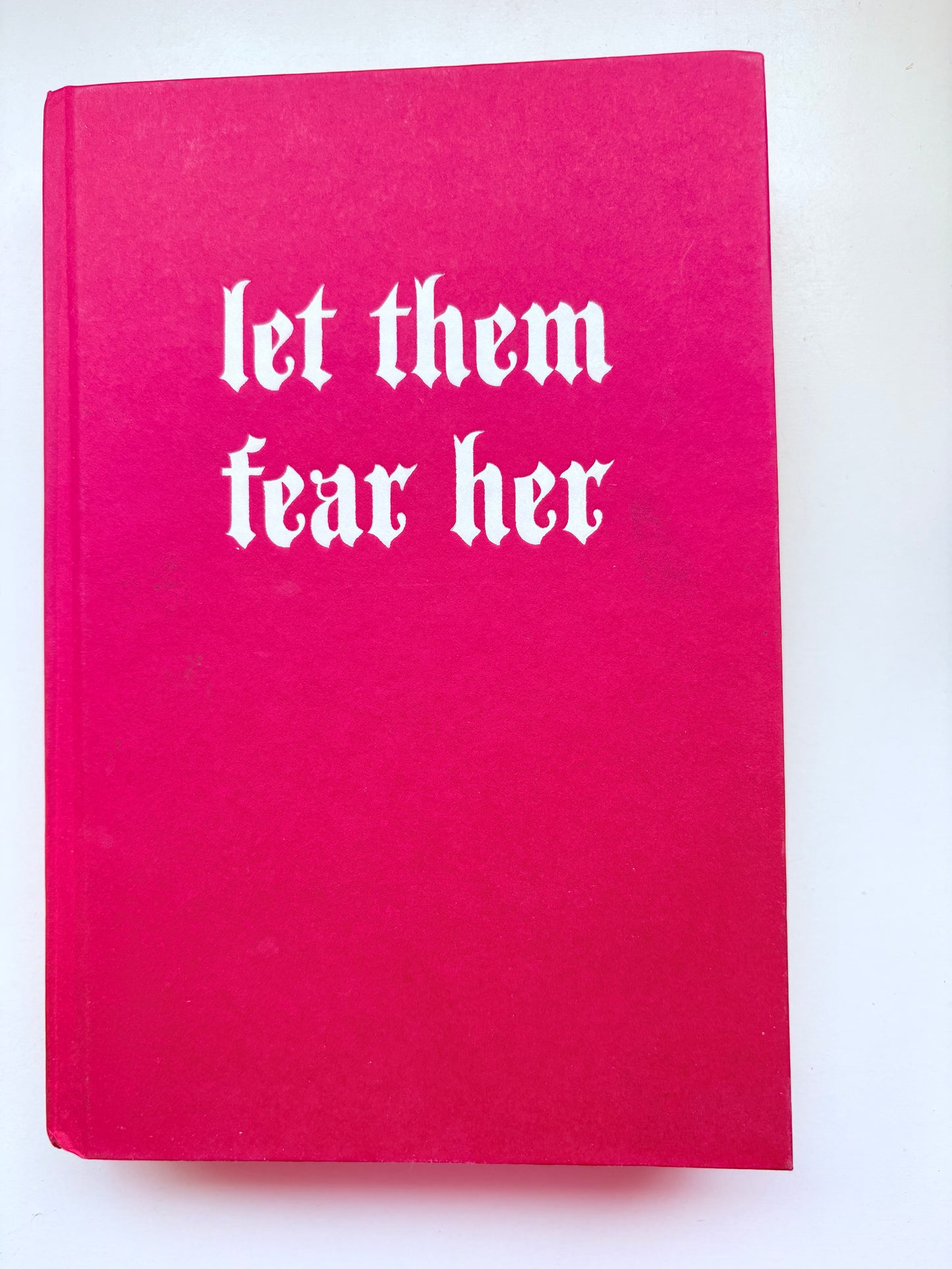 Pink book with white text 'let them fear her' on a white background