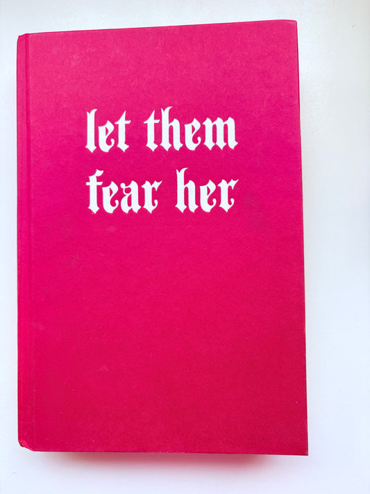 Pink book with white text 'let them fear her' on a white background