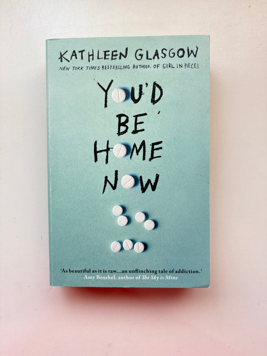 Book cover of 'You'd Be Home Now' by Kathleen Glasgow with pills on a light blue background
