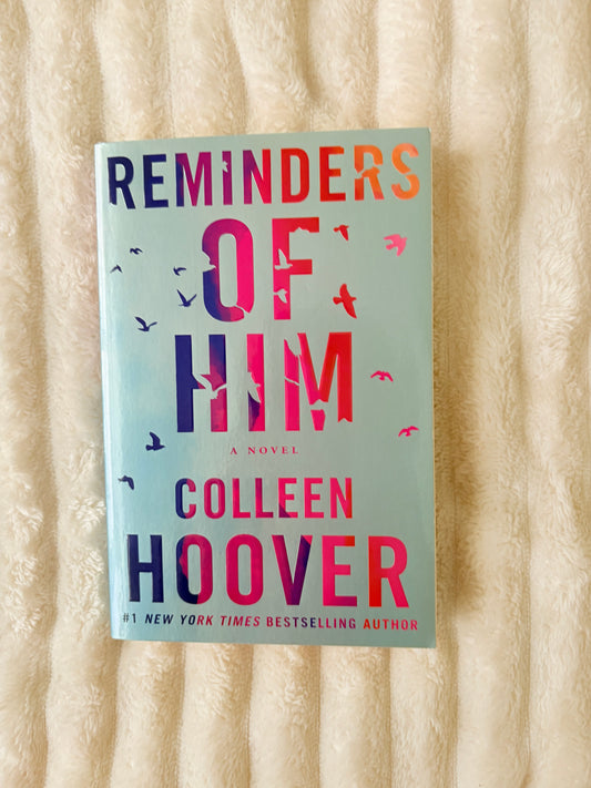 Book titled 'Reminders of Him' by Colleen Hoover on a wooden surface